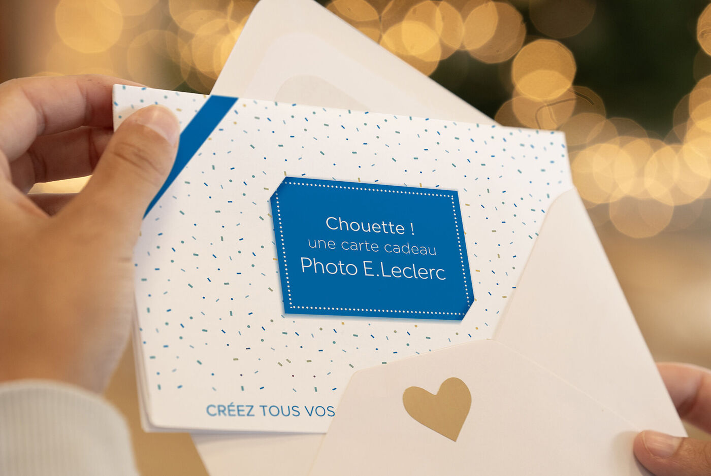Une main tient une carte de vœux avec un autocollant bleu et un cœur à l'intérieur de l'enveloppe blanche.