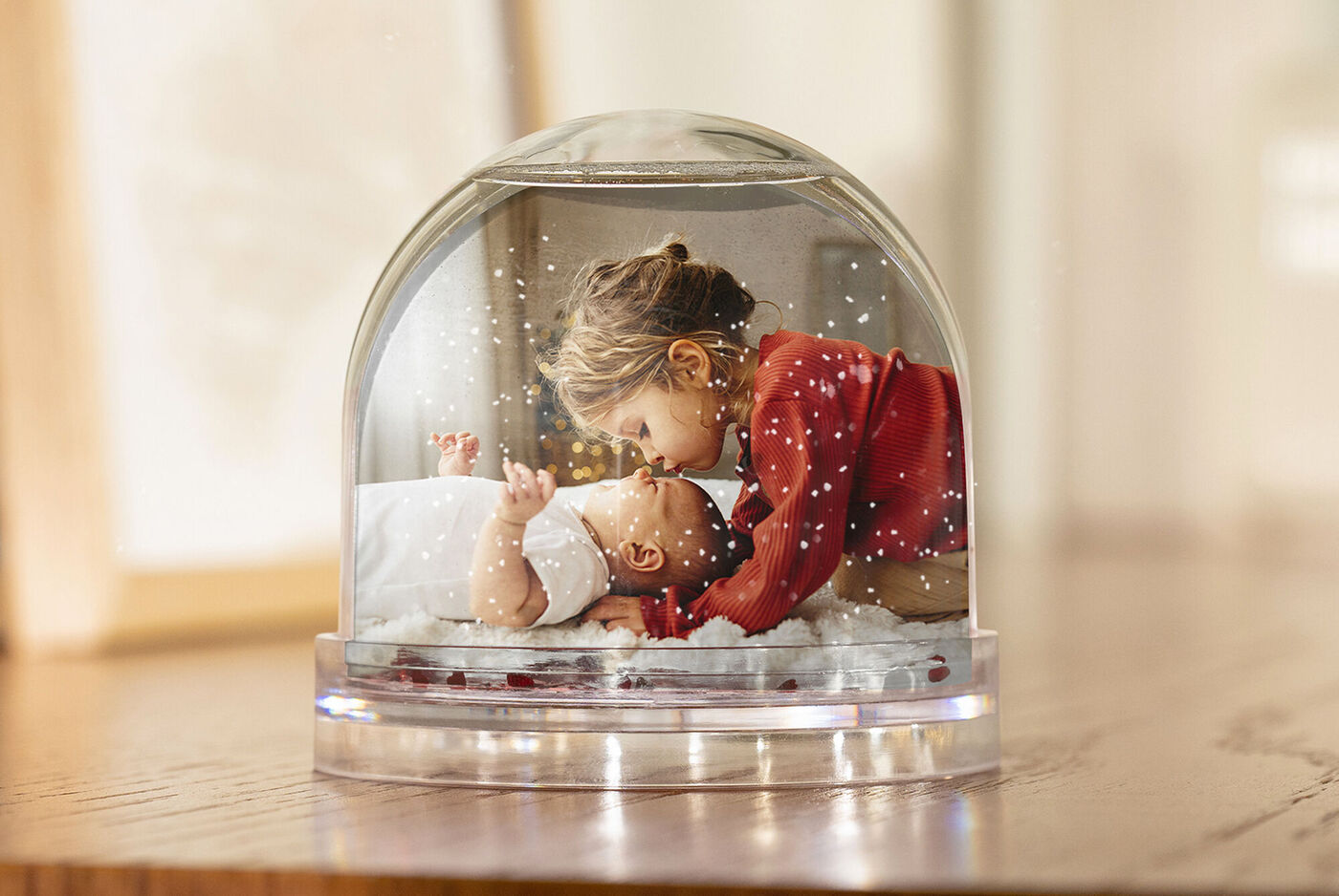 Deux enfants sous une boule à neige dans une pièce chauffée. L'aîné se penche doucement vers le cadet.