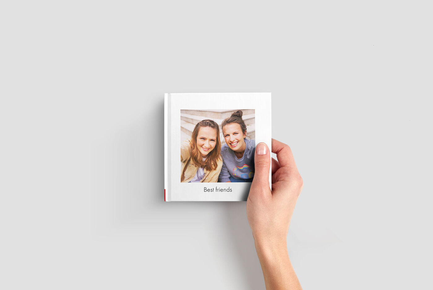 Une main tient un livre photo CEWE intitulé 'Meilleurs amis'.