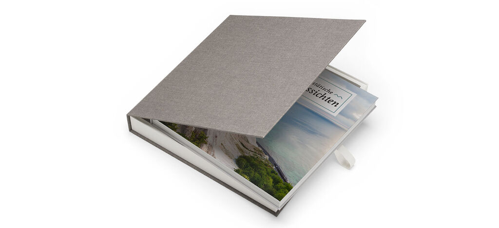 Un livre photo CEWE soigneusement conçu avec une couverture grise et des pages montrant un paysage de vacances.