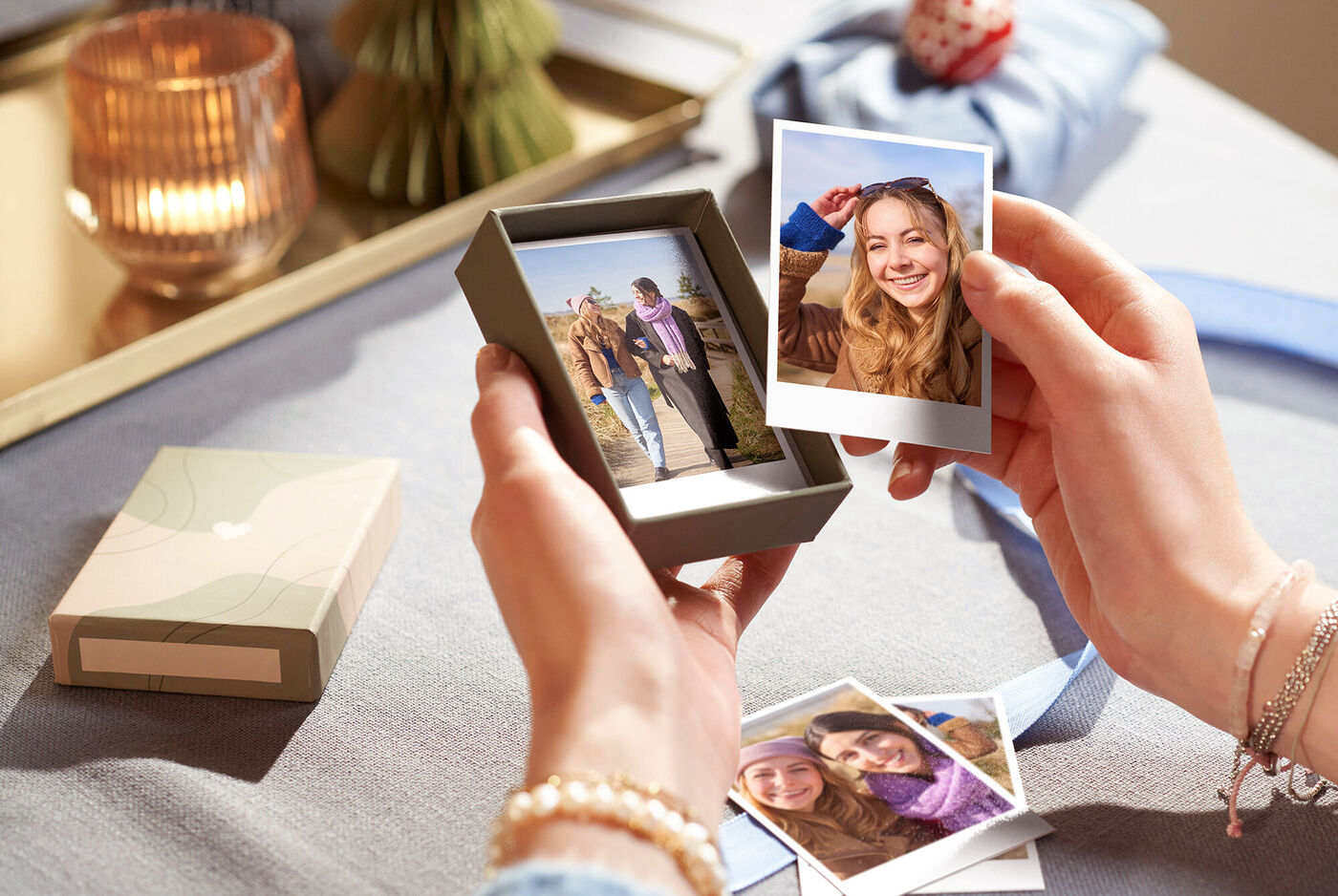 Une personne tient une boîte avec des tirages photo entourée d'autres photos et d'une déco élégante.